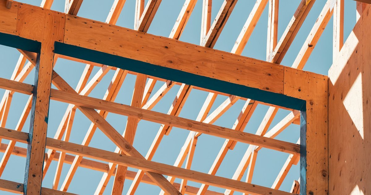 Timber wall framing and roof trusses of a house under construction against a blue sky.