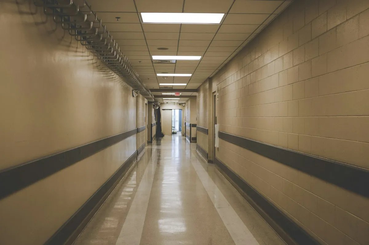 A long institutional corridor with block walls, rails along both sides and doorways set into the right-hand wall.