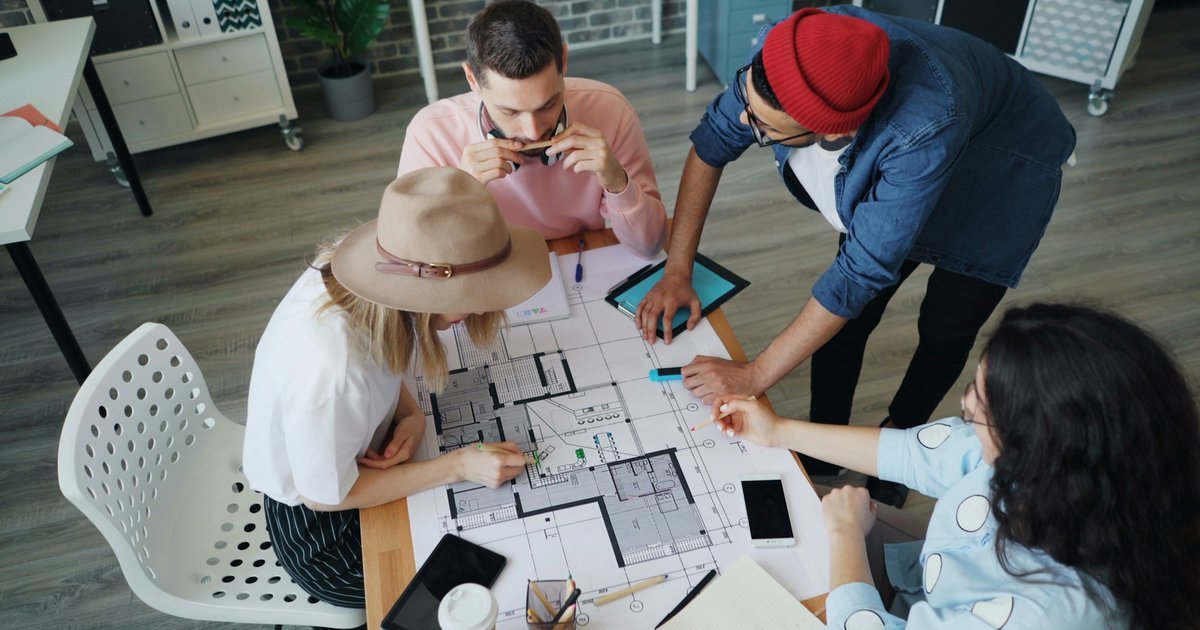 Four architects around a table reviewing a printed floor plan before deciding where AI fits.