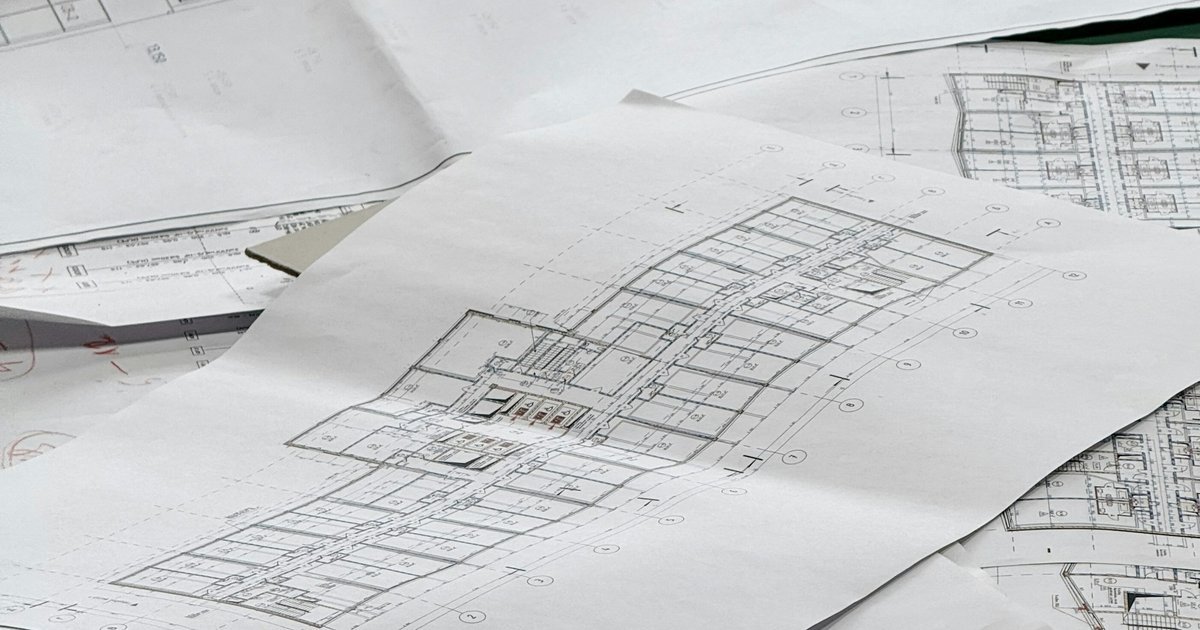 Architectural blueprints spread across a work surface, with printed floor plans and linework in view.