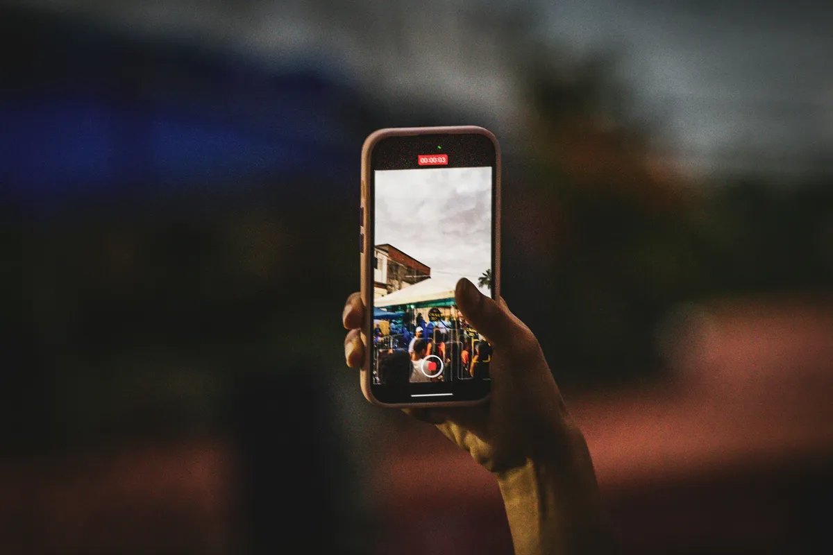 A hand holds up a phone to take a photo, with the camera view showing on the screen.